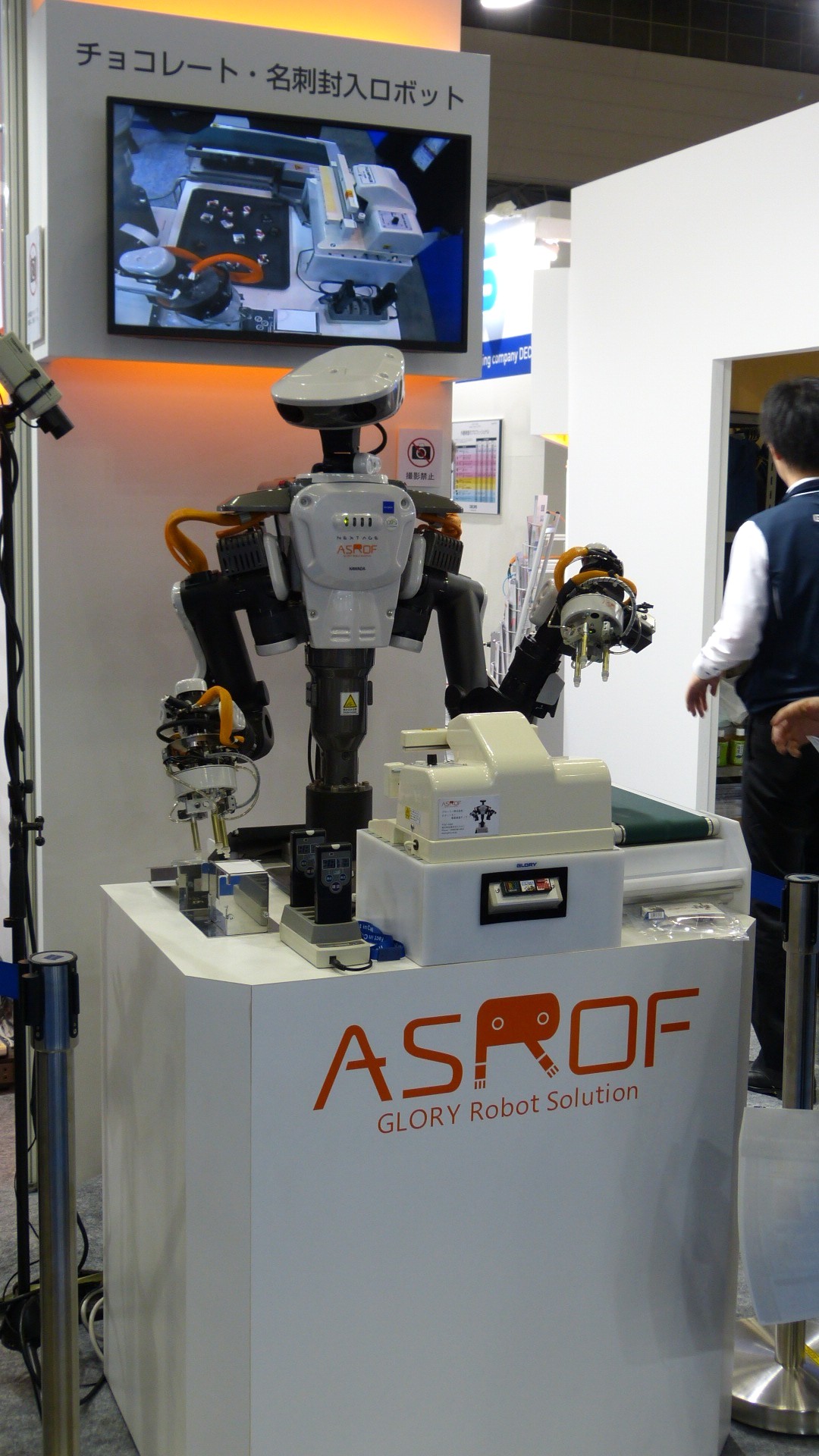 a robot without legs is mounted on a counter with the logo for Asrof glory robot solution.  A screen behind it shows its camera view of small objects.